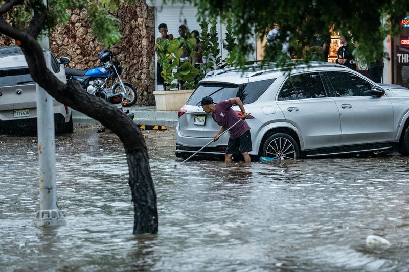 Person sweeping floodwater from a street outside homes